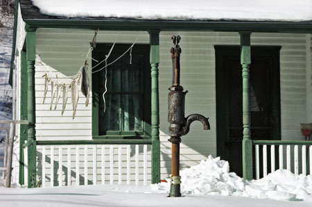 Hand operated well pump in front of porch with fish hanging to dry.